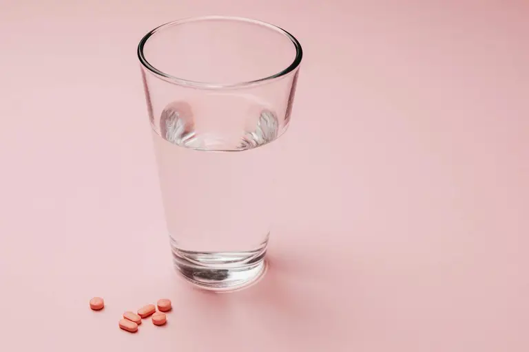 A row of supplement bottles next to a glass of water