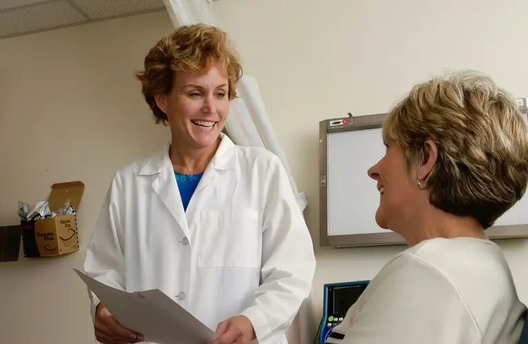 A middle-aged woman consulting with a female care team lead about perimenopause symptoms, discussing estradiol and progesterone levels for hormone therapy.
