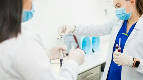 Two lab technicians handling blood sample tubes